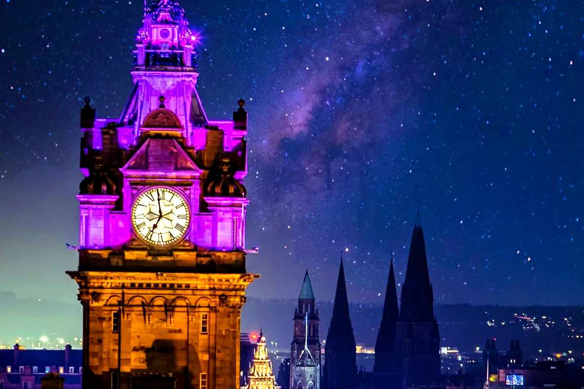 La torre dell'orologio del Balmoral illuminata e le guglie di Edimburgo sotto il cielo stellato