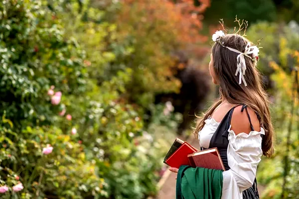 Una ragazza in abito d'epoca con dei libri, in un giardino di rose